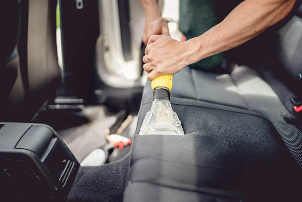 an interior detail cleaner using a wet vacuum to clean the back seats of a car